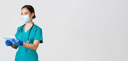 Covid-19, coronavirus disease, healthcare workers concept. Smiling friendly female nurse, physician in scrubs and rubber gloves provide patients with medical masks, white background photo