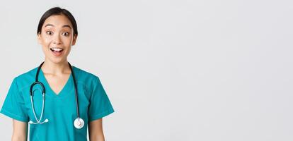 Healthcare workers, preventing virus, quarantine campaign concept. Happy and excited asian female doctor, physician in scrubs look amazed, hear awesome news, white background photo