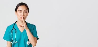 Healthcare workers, preventing virus, quarantine campaign concept. Sassy cute asian female doctor, physician shushing and winking coquettish, have secret, prepare surprise, asking keep quiet photo