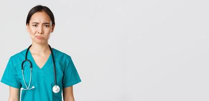 Healthcare workers, preventing virus, quarantine campaign concept. Close-up of skeptical and reluctant female asian physician, medical worker in scrubs looking displeased, white background photo