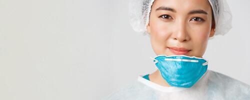 Covid-19, coronavirus disease, healthcare workers concept. Smiling, hopeful and exhausted asian female doctor having face damage from respirator, standing white background photo