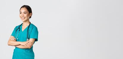 Covid-19, healthcare workers, pandemic concept. Side view of professional confident and hopeful asian female doctor, nurse looking assured away and smiling, standing in scrubs white background photo