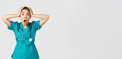 Covid-19, healthcare workers and preventing virus concept. Shocked and anxious asian female doctor in panic, grab head and screaming alarmed, have big problem, got in trouble, white background photo