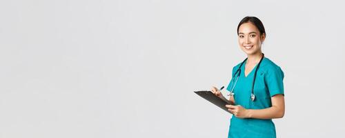 Healthcare workers, preventing virus, quarantine campaign concept. Smiling friendly female doctor, nurse in scrubs writing dorn results analysis at clipboard, standing white background photo