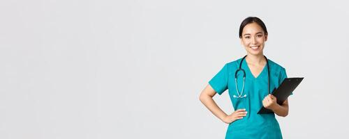 Healthcare workers, preventing virus, quarantine campaign concept. Smiling pleasant asian female physician, doctor during examination wearing scrubs and holding clipboard, white background photo