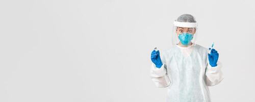 Covid-19, coronavirus disease, healthcare workers concept. Amazed and excited female asian doctor, infectionist in personal protective equipment, holding syringe and ampoule with vaccine photo