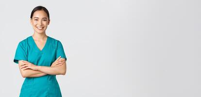 Covid-19, healthcare workers, pandemic concept. Confident smiling asian doctor, female nurse in scrubs standing determined, cross arms chest over white background. Doctor ready for shift in clinic photo