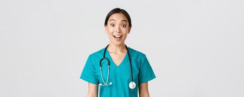 Healthcare workers, preventing virus, quarantine campaign concept. Happy and excited asian female doctor, physician in scrubs look amazed, hear awesome news, white background photo