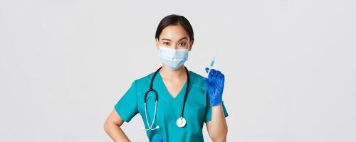 Covid-19, coronavirus disease, healthcare workers concept. Sassy cute asian female nurse, intern in medical mask and gloves holding syringe with vaccine, ready to make shot, white background photo