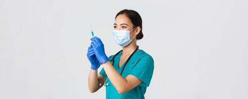 Covid-19, coronavirus disease, healthcare workers concept. Side view of confident smiling asian female physician, nurse prepare syringe with vaccine for flu shot, standing white background photo