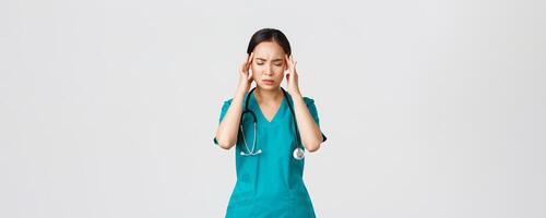Covid-19, healthcare workers, pandemic concept. Overworked and tired young asian female nurse close eyes, grimacing from headache, feel dizzy, night shift with coronavirus patients, white background photo