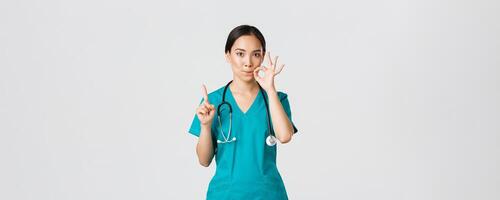 Covid-19, healthcare workers, pandemic concept. Serious-looking worried asian female nurse, physician asking keep secret, shaking finger and showing mouth seal, zipping lips gesture photo
