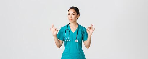 Covid-19, healthcare workers, pandemic concept. Impressed good-looking asian female nurse in scrubs, doctor show okay gesture and nod in approval, praise excellent choice, compliment someone photo