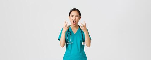 COVID-19, cuidado de la salud trabajadores y prevenir virus concepto. enojado enfadado asiático hembra enfermero, médico perdiendo temperamento, estresado médico gritos en enojo, mirando enojado y agresivo foto