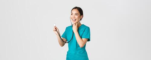 Covid-19, healthcare workers and preventing virus concept. Smiling friendly-looking asian female doctor listening to patient lungs during daily checkup, using stethoscope, white background photo