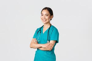 Covid-19, healthcare workers, pandemic concept. Professional confident, smiling asian female doctor, nurse in scrubs with stethoscope for examinations, cross arms and look at camera photo