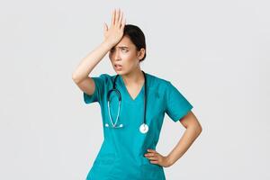 Covid-19, healthcare workers, pandemic concept. Annoyed and pissed-off asian female doctor in scrubs slap forehead, facepalm and eyeroll from someone stupid, tired standing white background photo