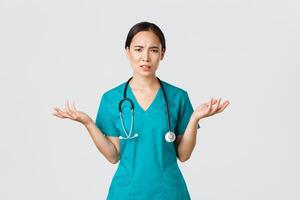 Covid-19, healthcare workers, pandemic concept. Confused and disappointed asian nurse, female doctor in scrubs spread hands sideways and shrugging bothered, cant understand, asking why photo