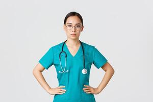 Covid-19, healthcare workers, pandemic concept. Confident determined asian female nurse helping patients, working with coronavirus disease, looking ready, wearing scrubs and glasses, white background photo