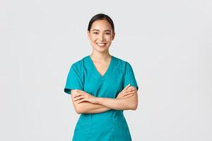 Covid-19, healthcare workers, pandemic concept. Confident smiling asian doctor, female nurse in scrubs standing determined, cross arms chest over white background. Doctor ready for shift in clinic photo