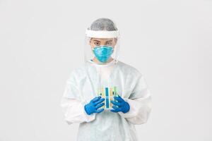 Covid-19, coronavirus disease, healthcare workers concept. Serious-looking careful asian female tech lab worker, researcher in personal protective equipment, holding test-tubes with vaccine photo