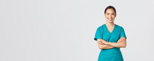 Covid-19, healthcare workers, pandemic concept. Confident smiling asian doctor, female nurse in scrubs standing determined, cross arms chest over white background. Doctor ready for shift in clinic photo