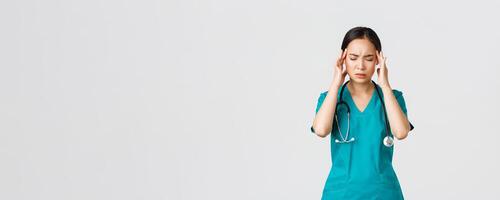 Covid-19, healthcare workers, pandemic concept. Overworked and tired young asian female nurse close eyes, grimacing from headache, feel dizzy, night shift with coronavirus patients, white background photo