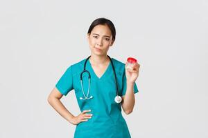 Healthcare workers, preventing virus, quarantine campaign concept. Skeptical and displeased asian female physician, nurse do not recommend medication, smirk reluctant and show pills, white background photo