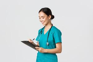 Healthcare workers, preventing virus, quarantine campaign concept. Beautiful smiling asian doctor, nurse running checkup in hospital, looking at clipboard with patient results, examine people photo