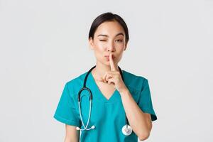 Healthcare workers, preventing virus, quarantine campaign concept. Sassy cute asian female doctor, physician shushing and winking coquettish, have secret, prepare surprise, asking keep quiet photo