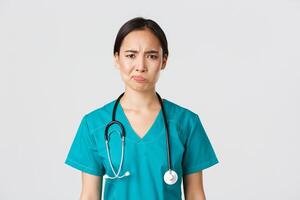 Healthcare workers, preventing virus, quarantine campaign concept. Close-up of skeptical and reluctant female asian physician, medical worker in scrubs looking displeased, white background photo