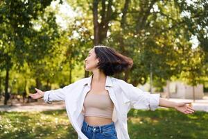 libertad y personas concepto. contento joven asiático mujer bailando en parque alrededor árboles, sonriente y disfrutando sí misma foto