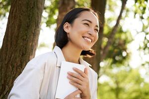 Romantic smiling girl reading book in park or foret, sitting under tree shade on sunny day, relaxing on fresh air surrounded by nature photo