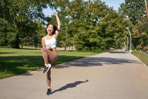 Happy asian girl celebrating victory, saying yes, finish running, workout in park with excitement and joy photo