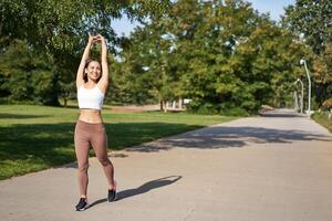 Smiling Asian girl stretching after good workout in park, listening music in wireless headphones, jogging outdoors photo