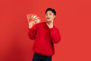 Excited handsome Asian man holding red envelopes isolated red background photo