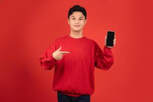 Young handsome man pointing to his mobile phone in hand isolated on red background photo