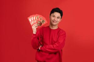 Smiling handsome Asian man holding red Ang Pao in studio isolated red background for Chinese new year concepts photo