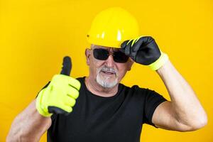 trabajador con guantes y casco demostración pulgar arriba en contra amarillo antecedentes foto