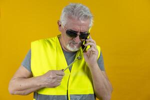 Mature worker talking on smartphone isolated on yellow background photo