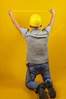 craftsman worker with hard hat is measuring with a tape measure isolated on yellow background photo