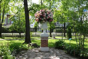 A white flowerpot on a pedestal with artificial flowers stands in the middle of the park. photo