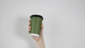 In his hand is a green paper cup with a brown lid on a white background. A place for your text. photo