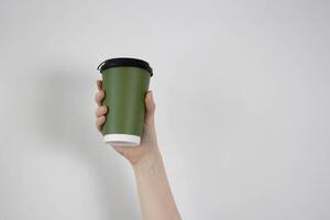 In his hand is a green paper cup with a brown lid on a white background. A place for your text photo