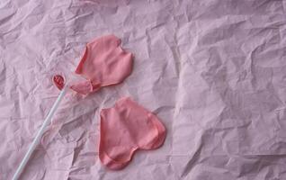 A burst pink balloon heart on a stick lies on a background of pink crumpled paper. A place for your text photo