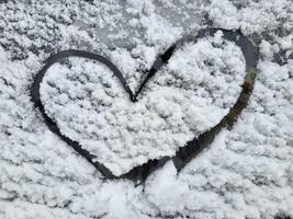 corazón dibujado en un coche parabrisas cubierto con Fresco Navidad nieve. foto