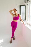 Woman in vibrant pink sports outfit standing next to window with palm on forehead photo