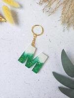 green glitter letters with beads. Golden keychain on white paper background with dried flowers. Top view. Resin craft. photo