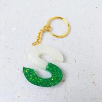 green glitter letters with beads. Golden keychain on white paper background with dried flowers. Top view. Resin craft. photo