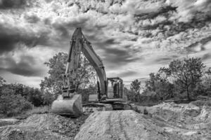 Crawler excavator during earthmoving works on construction site in black and white photo